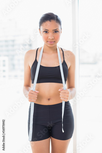 Stern dark haired model in sportswear holding a measuring tape