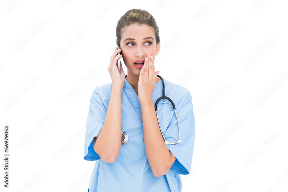 Astonished brown haired nurse in blue scrubs making a phone call Astonished brown haired nurse in blue scrubs making a phone call