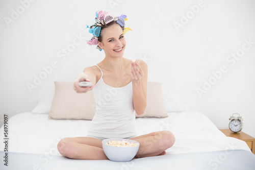 Delighted natural brown haired woman in hair curlers eating popc