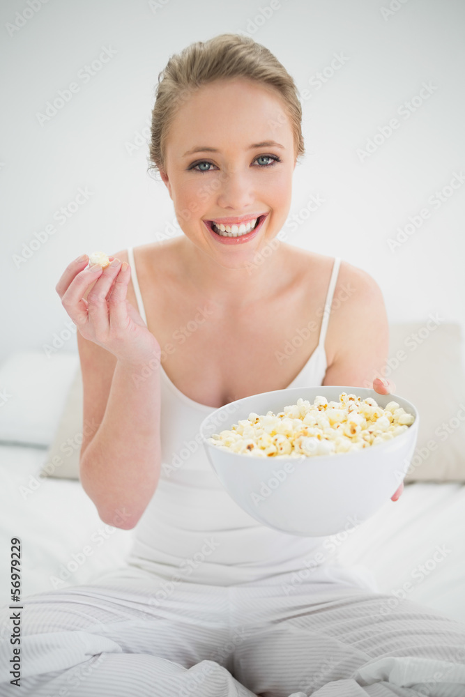 Natural cheerful blonde holding bowl of popcorn on bed Natural cheerful blonde holding bowl of popcorn on bed
