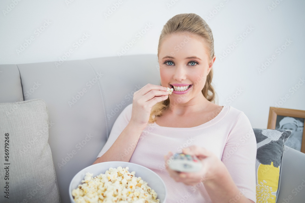 Casual smiling blonde holding remote and eating popcorn Casual smiling blonde holding remote and eating popcorn
