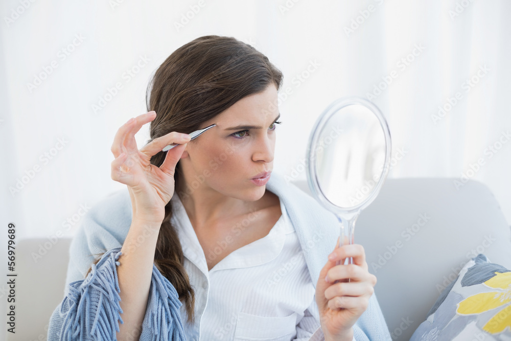 Focused casual brown haired woman in white pajamas plucking her Focused casual brown haired woman in white pajamas plucking her