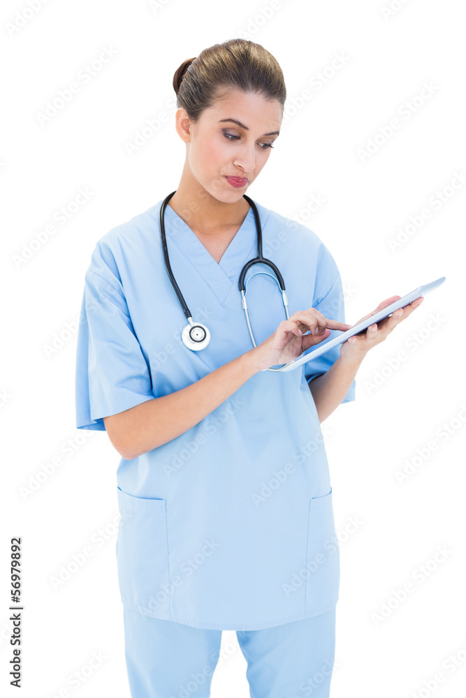 Thoughtful brown haired nurse in blue scrubs using a tablet pc Thoughtful brown haired nurse in blue scrubs using a tablet pc