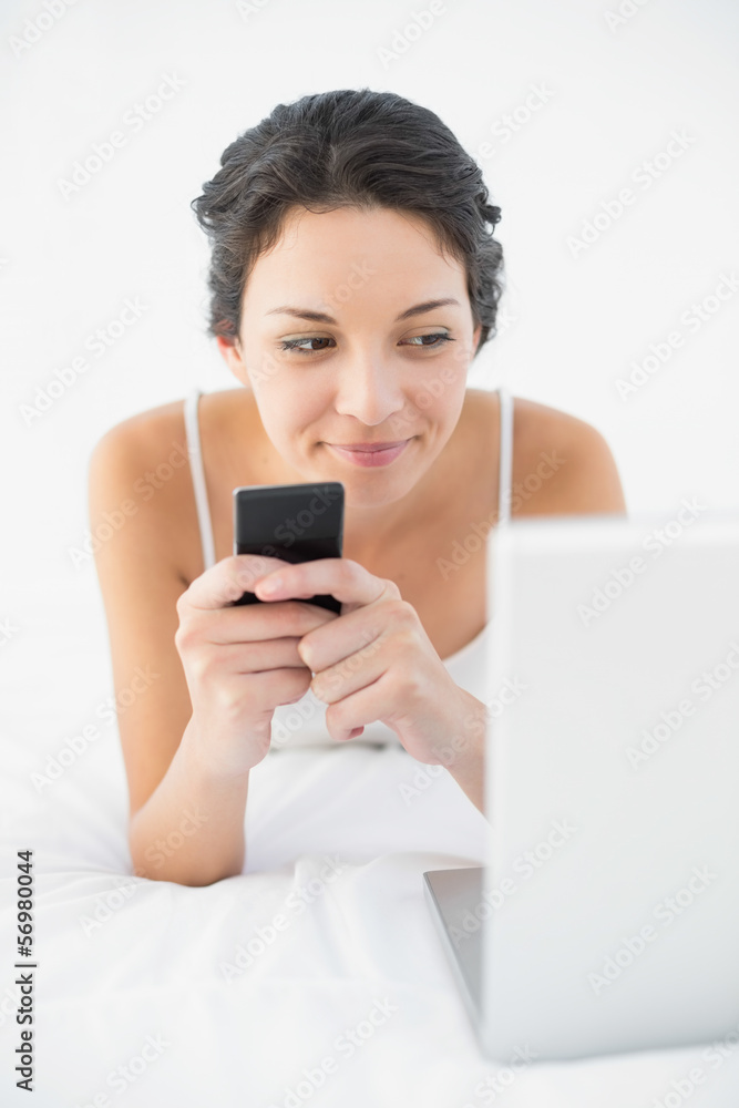 Peaceful casual brunette in white pajamas using her mobile phone Peaceful casual brunette in white pajamas using her mobile phone