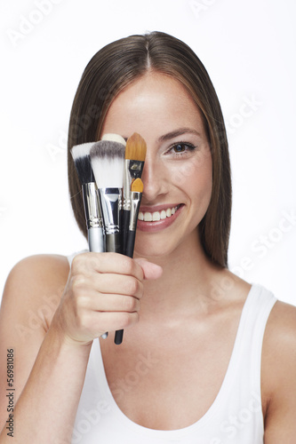 Young woman holding make-up brushes against white background