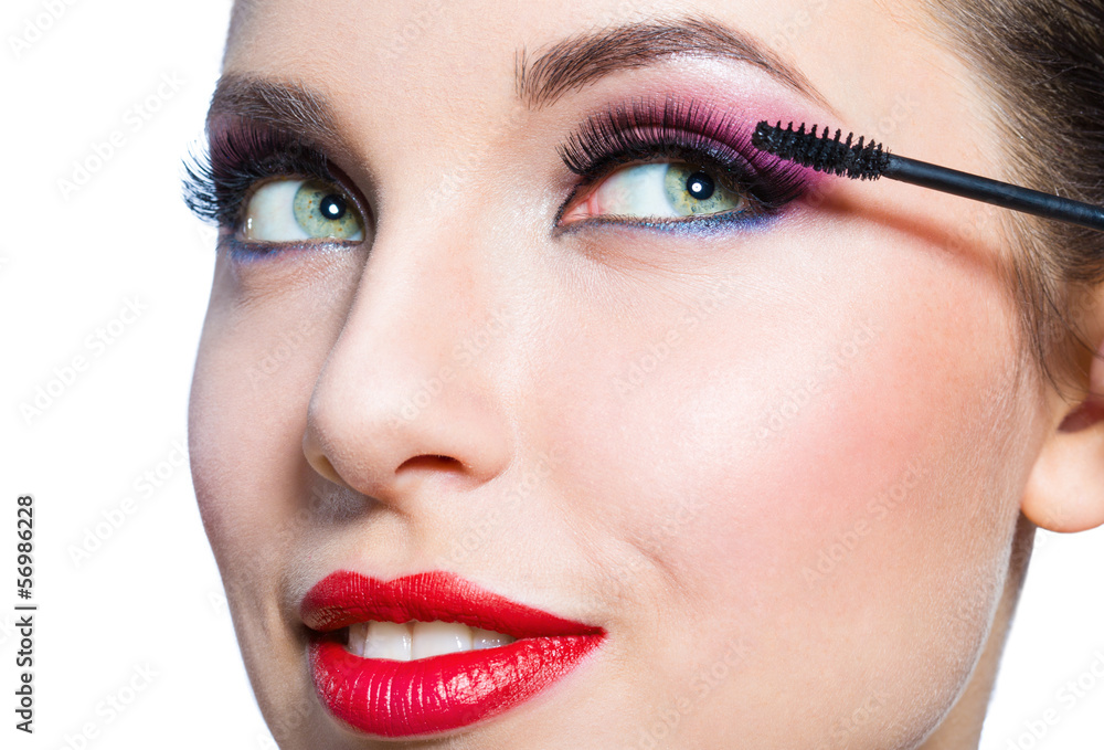 Headshot of female with bright makeup applying mascara