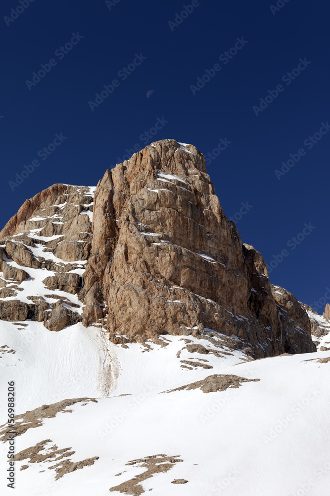 Snowy rock and cloudless sky with moon