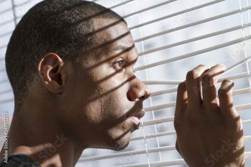 Nervous young black man looking out window, horizontal