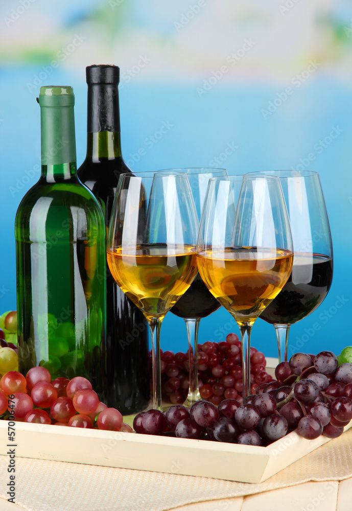 Wine bottles and glasses of wine on tray, on bright background