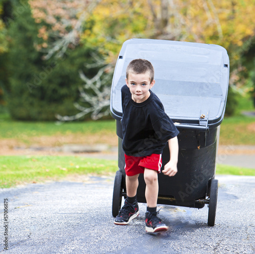 Photo Young boy bringing trash can up the driveway