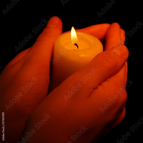 Burning candle in hands isolated on black
