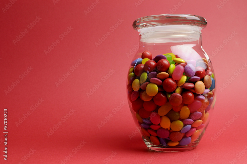 Glass candy jar against red background with copy space Glass candy jar against red background with copy space
