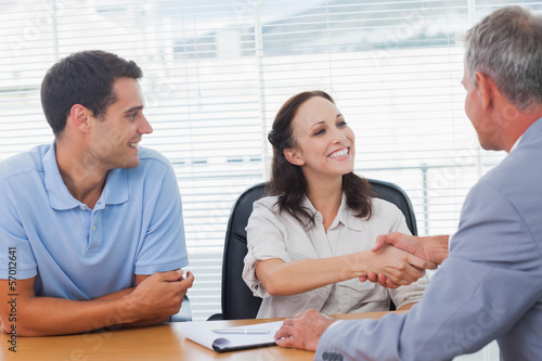 Pretty woman with her husband shaking hands with estate agent