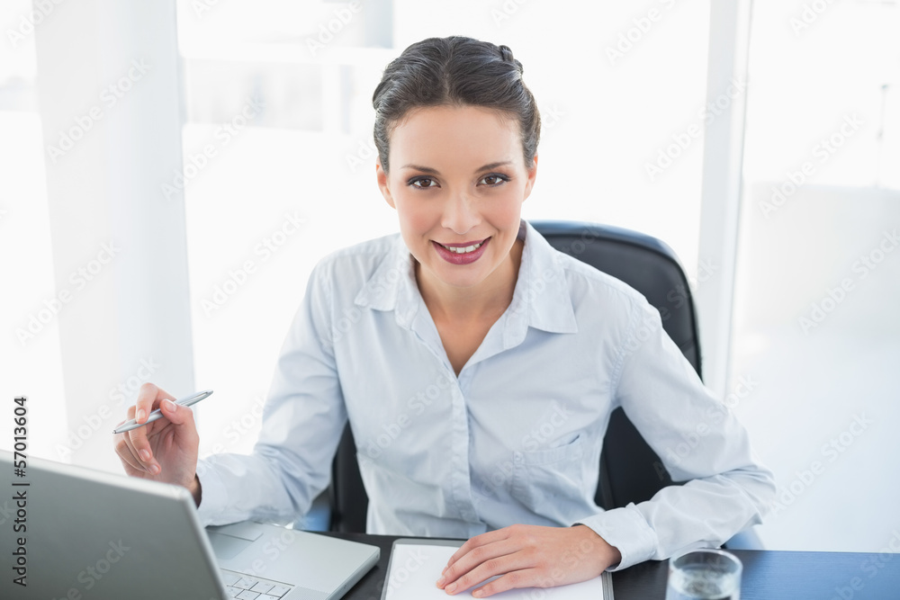 Happy stylish brunette businesswoman taking notes and looking at Happy stylish brunette businesswoman taking notes and looking at