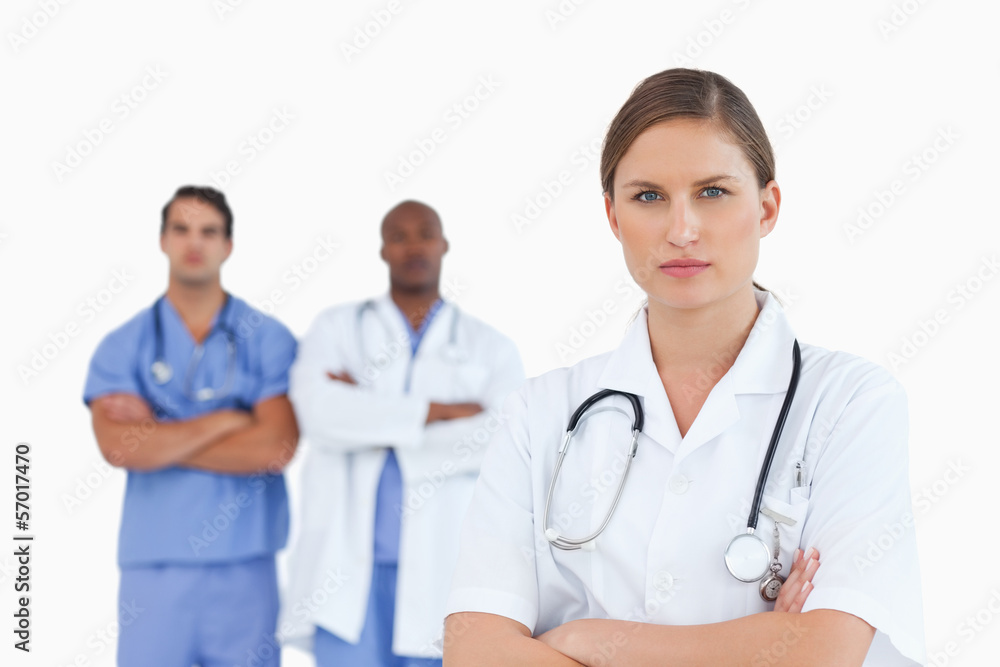 Female doctor with folded arms and male colleagues behind her Female doctor with folded arms and male colleagues behind her
