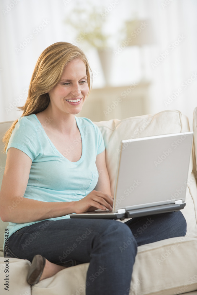 Woman Using Laptop While Sitting On Sofa Woman Using Laptop While Sitting On Sofa