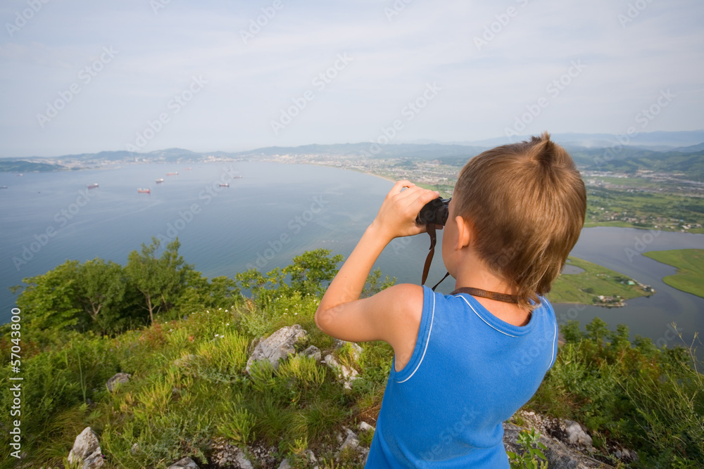 Boy looking through binoculars from the top of the mountain Boy looking through binoculars from the top of the mountain