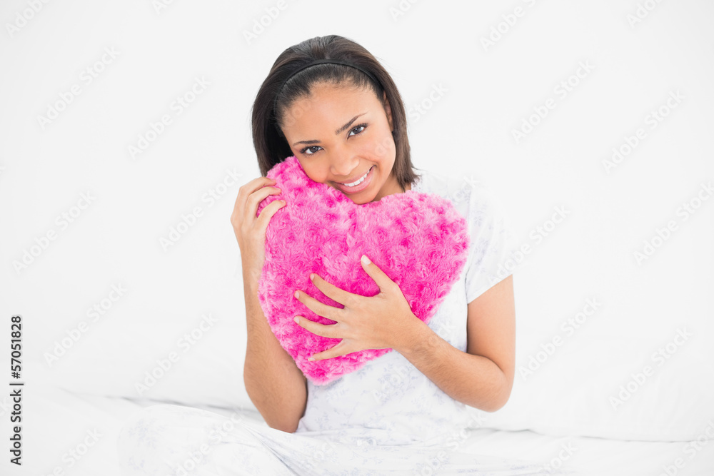 Amused young dark haired model cuddling a heart-shaped pillow Amused young dark haired model cuddling a heart-shaped pillow