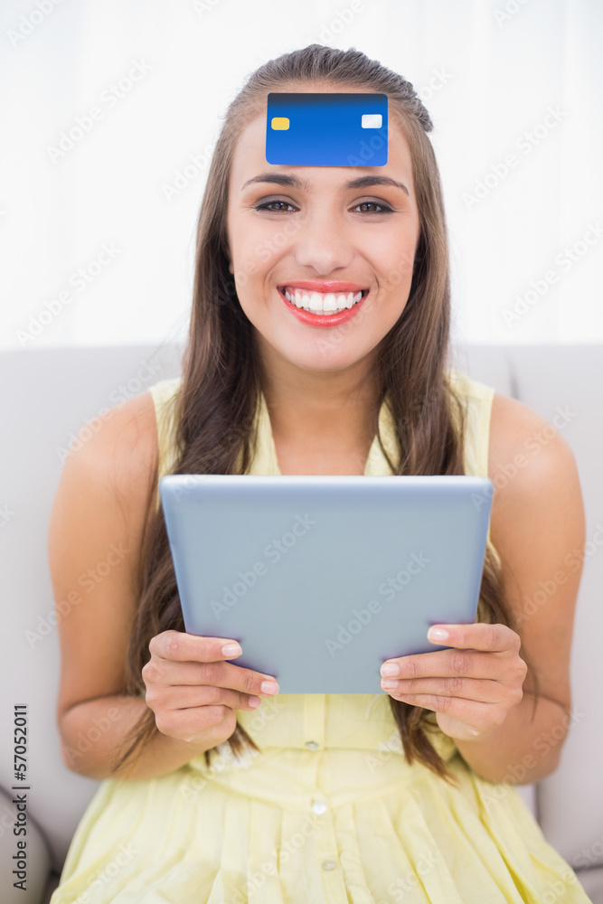 Happy brunette with credit card on forehead holding tablet Happy brunette with credit card on forehead holding tablet