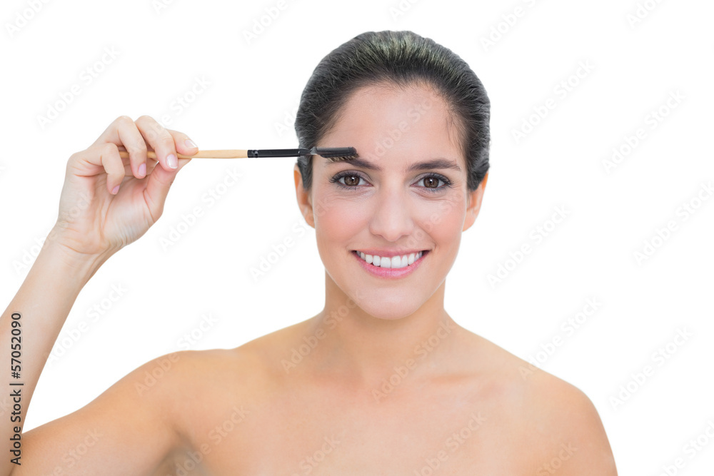 Smiling bare brunette using eyebrow brush