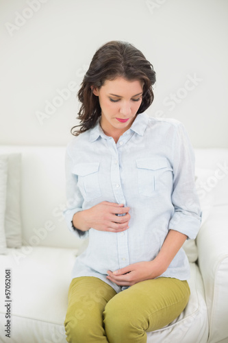 Thoughtful pregnant brown haired woman holding her belly