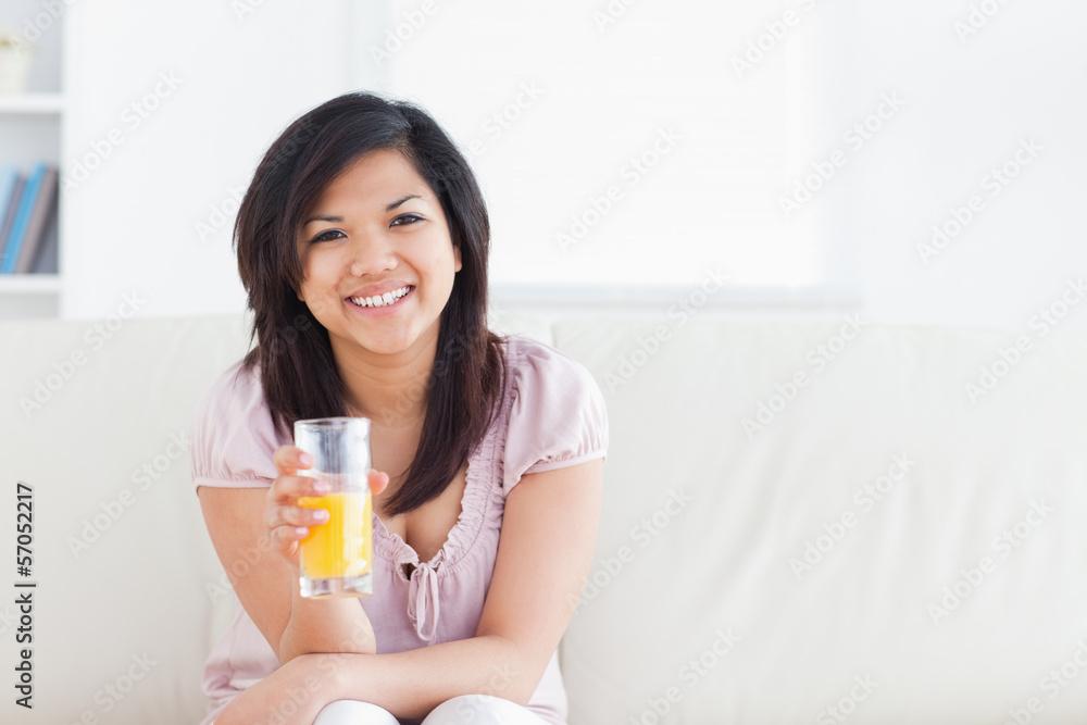Woman smiling and sitting in a couch while holding a glass of or Woman smiling and sitting in a couch while holding a glass of or
