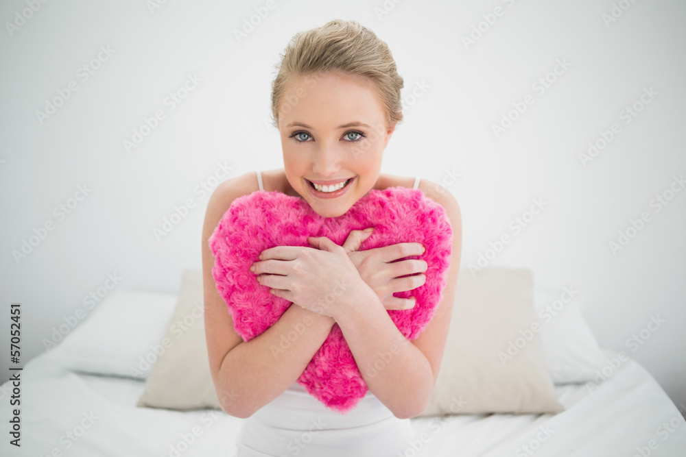 Natural smiling blonde holding heart pillow Natural smiling blonde holding heart pillow