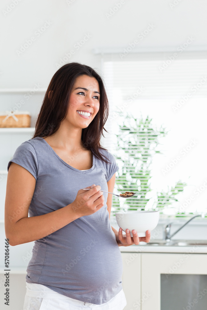 Beautiful pregnant woman enjoying a bowl of cereals while standi