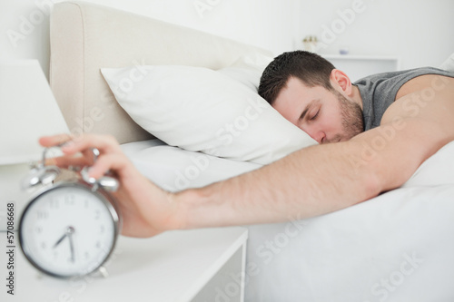 Sleeping handsome man being awakened by an alarm clock