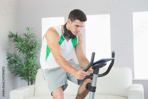 Sporty handsome man training on exercise bike using tablet