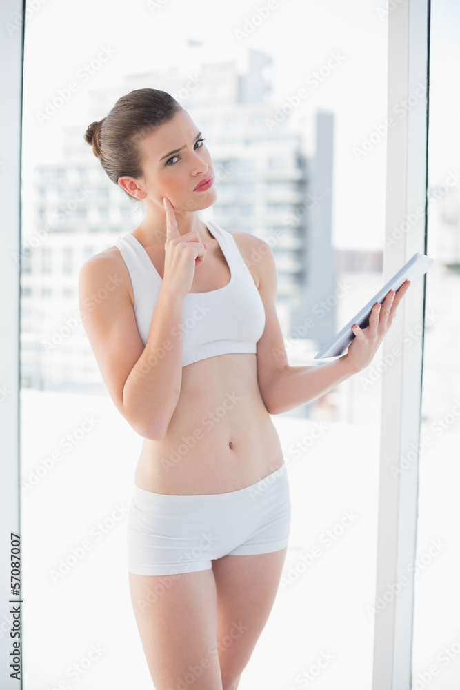 Thoughtful fit brown haired model in sportswear using a tablet p