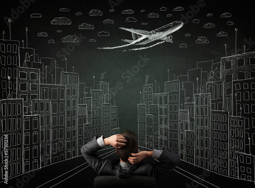 Businessman sitting in front of a cityscape drawing on a chalkbo