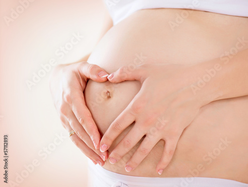 Pregnant Woman holding hands in a heart shape on her baby bump #57112893