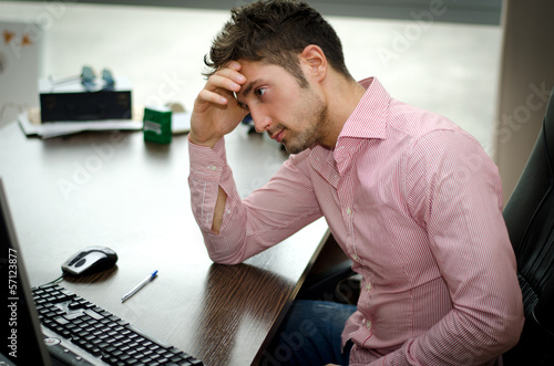 Preoccupied, worried young male worker staring at computer