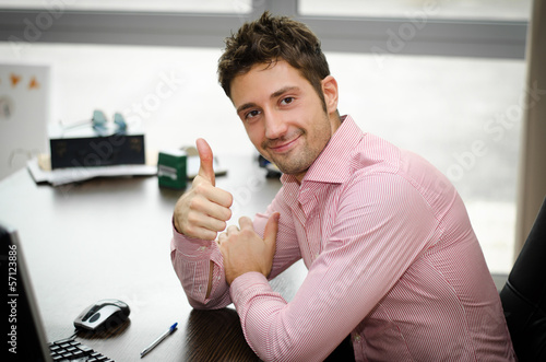 Fotografie Cheerful office worker at desk doing thumb up sign and smiling