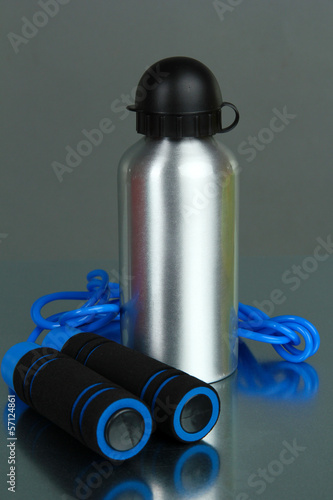 Sports bottle and skipping rope on grey background