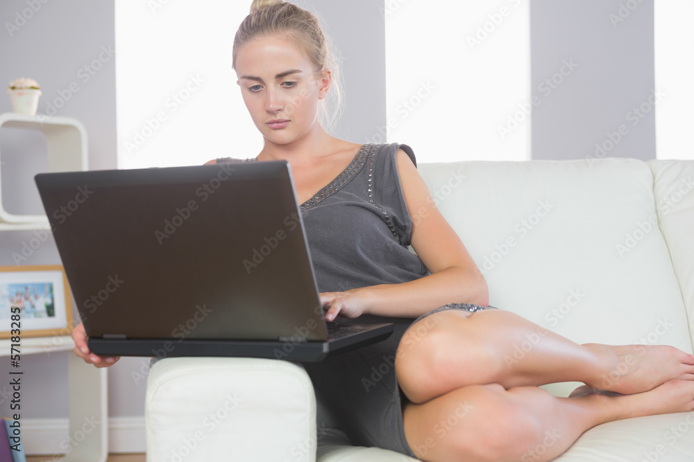 Casual stern blonde relaxing on couch using laptop Casual stern blonde relaxing on couch using laptop