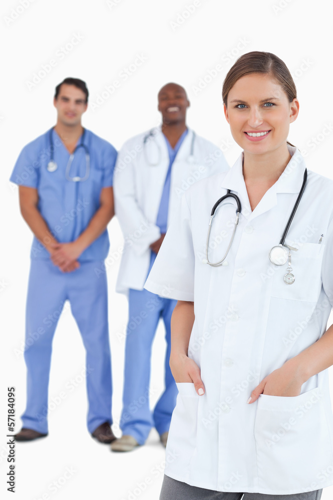Smiling female doctor with male colleagues behind her Smiling female doctor with male colleagues behind her