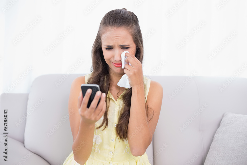 Crying attractive brunette holding mobile phone and tissue Crying attractive brunette holding mobile phone and tissue