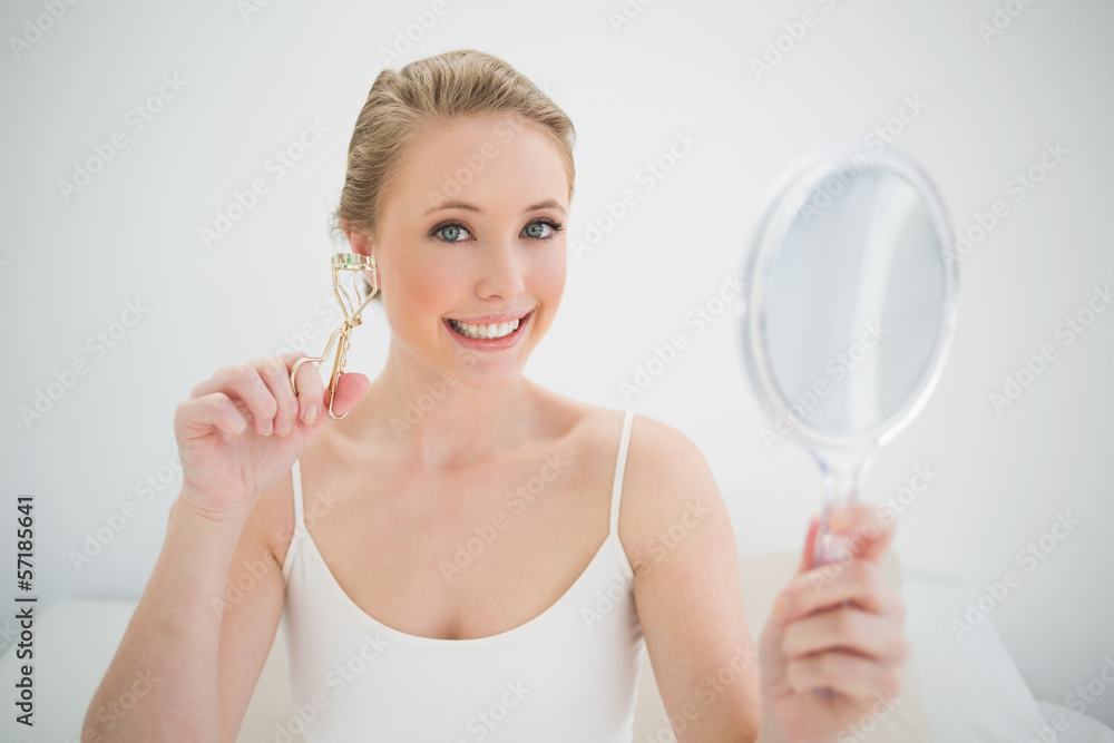 Natural smiling blonde holding mirror and eyelash curler Natural smiling blonde holding mirror and eyelash curler