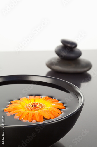 Orange gerbera floating on a black bowl and a stack of black peb photo