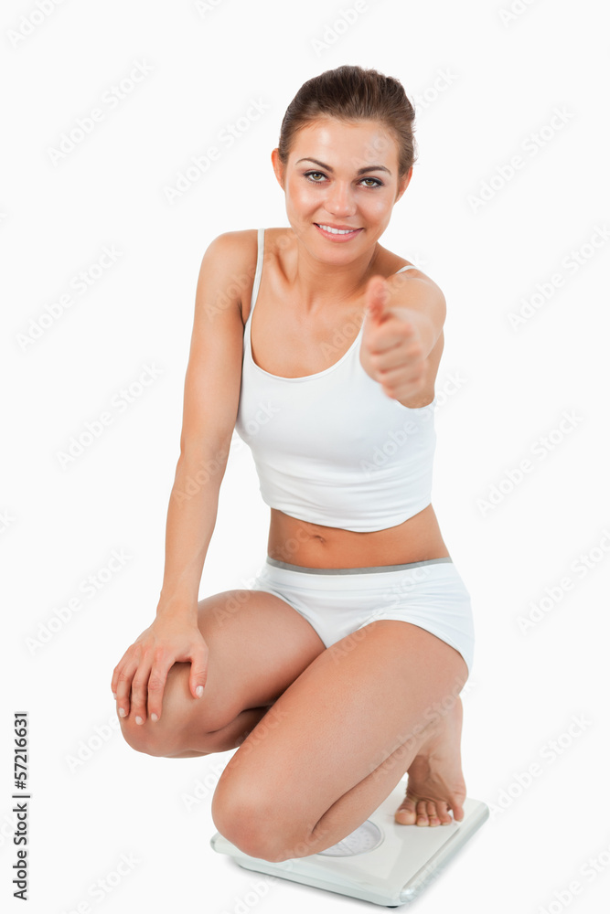 Portrait of a thin woman squatting on scales with the thumb up Portrait of a thin woman squatting on scales with the thumb up