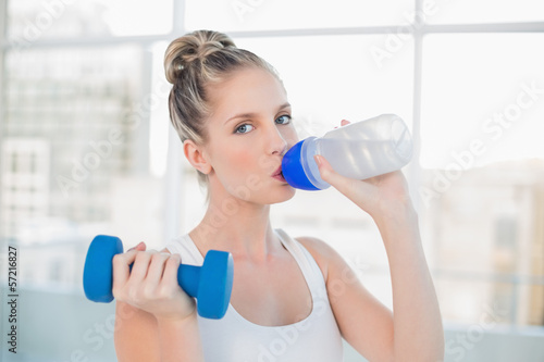 Sporty blonde drinking water while lifting dumbbell