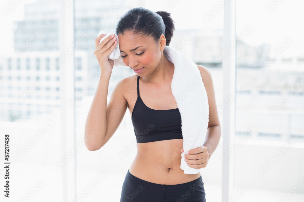 Tired dark haired model in sportswear drying herself with a towe