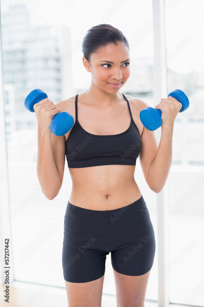 Fit dark haired model in sportswear exercising with dumbbells