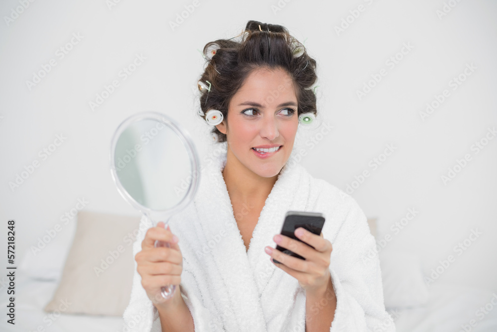 Pensive natural brunette holding mirror and smartphone