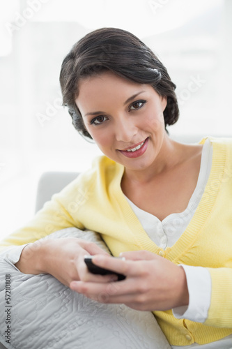 Happy casual brunette in yellow cardigan texting with a mobile p