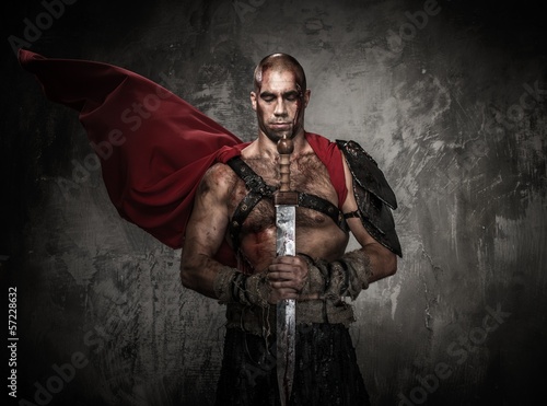 Wounded gladiator holding sword covered in blood with both hands