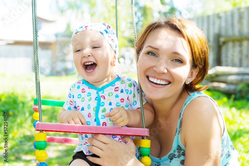 Happy mother with laughing baby sits on swing