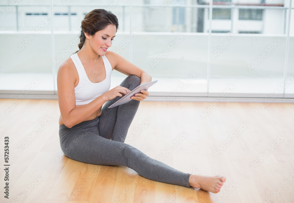 Sporty happy brunette using tablet sitting on the floor Sporty happy brunette using tablet sitting on the floor